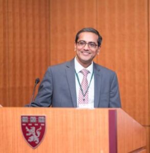 A man in a suit smiling behind a podium with a Harvard crest.