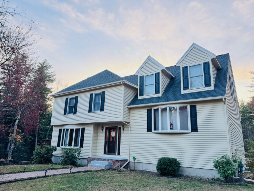 Large two-story house with beige siding and blue shutters under a blue sky.