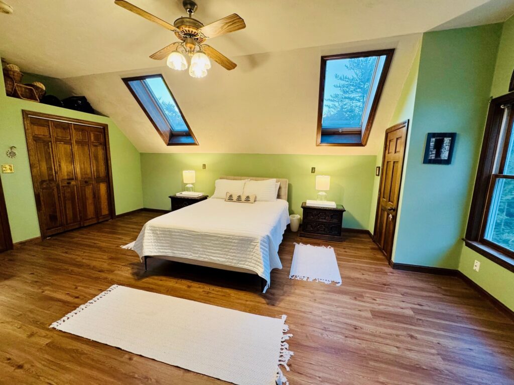 Cozy bedroom with skylights, wooden floors, and a ceiling fan.